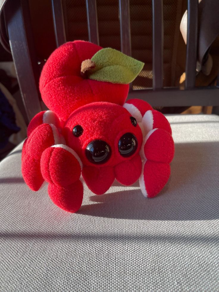 a red stuffed crab with a green leaf on its head sitting on a chair cushion