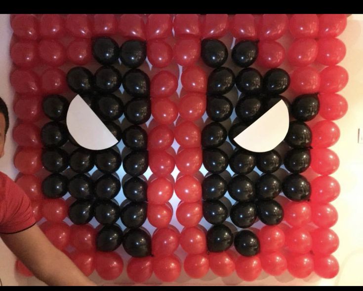 a man standing in front of a wall made out of red and black plastic balls