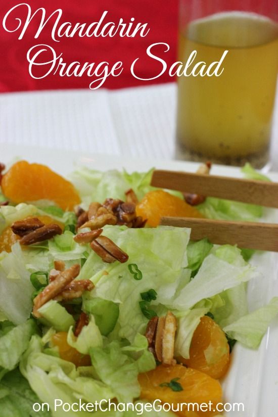 a salad with oranges and pecans is on a white plate next to a drink