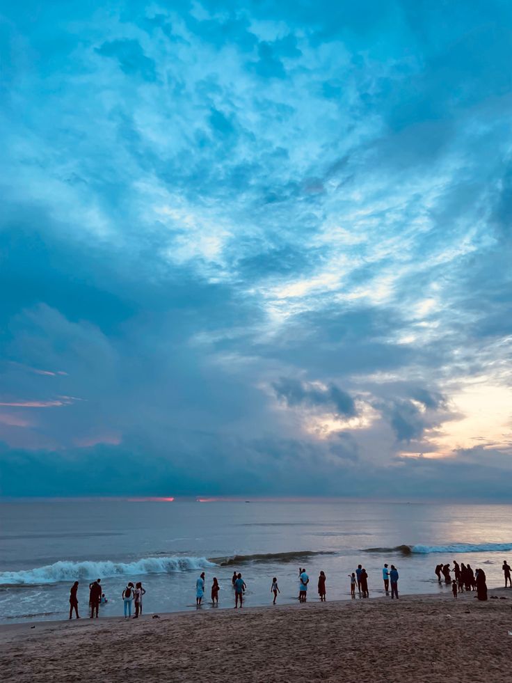 a group of people standing on top of a beach next to the ocean under a cloudy sky