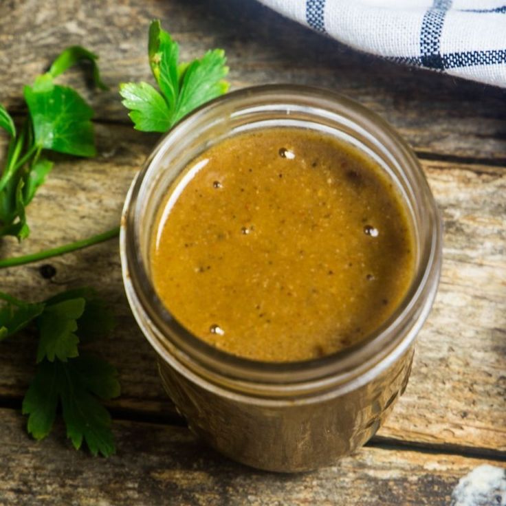 a jar filled with brown liquid sitting on top of a wooden table next to green leaves