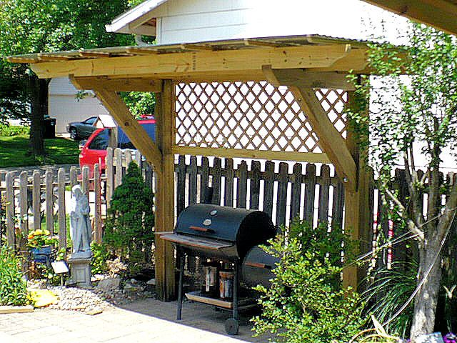 an outdoor bbq grill in the middle of a yard with a wooden fence around it