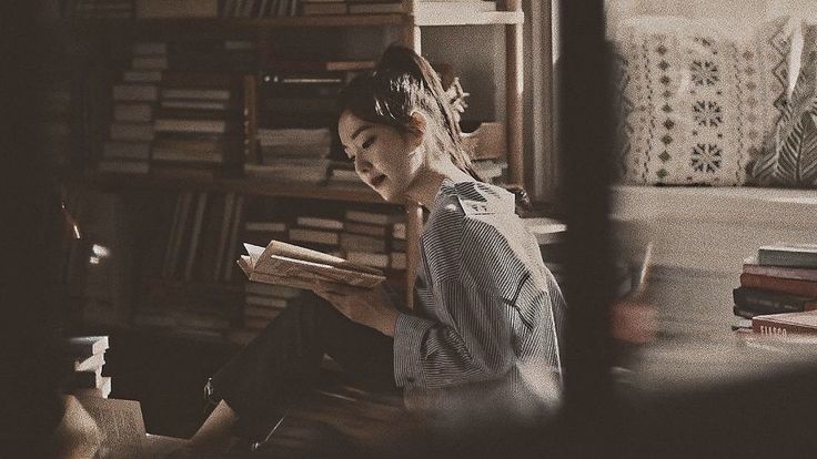 a woman sitting on the floor reading a book in front of a bookshelf