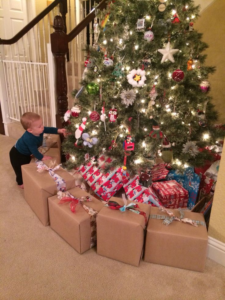 a small child reaching for presents under a christmas tree in front of a stair case