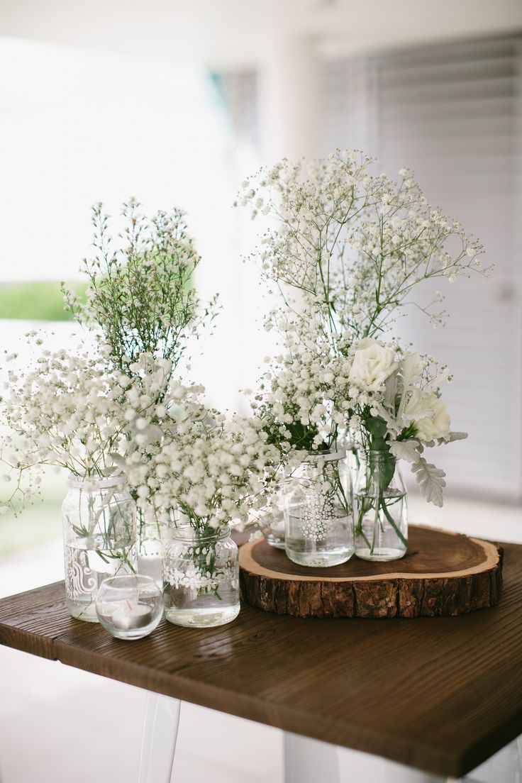 three vases filled with white flowers sitting on top of a wooden table next to each other