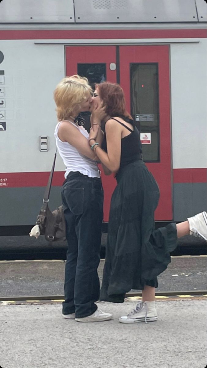 two women kissing each other in front of a train