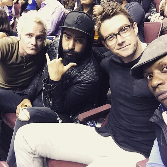 three men sitting next to each other at a sporting event, one with his finger up in the air