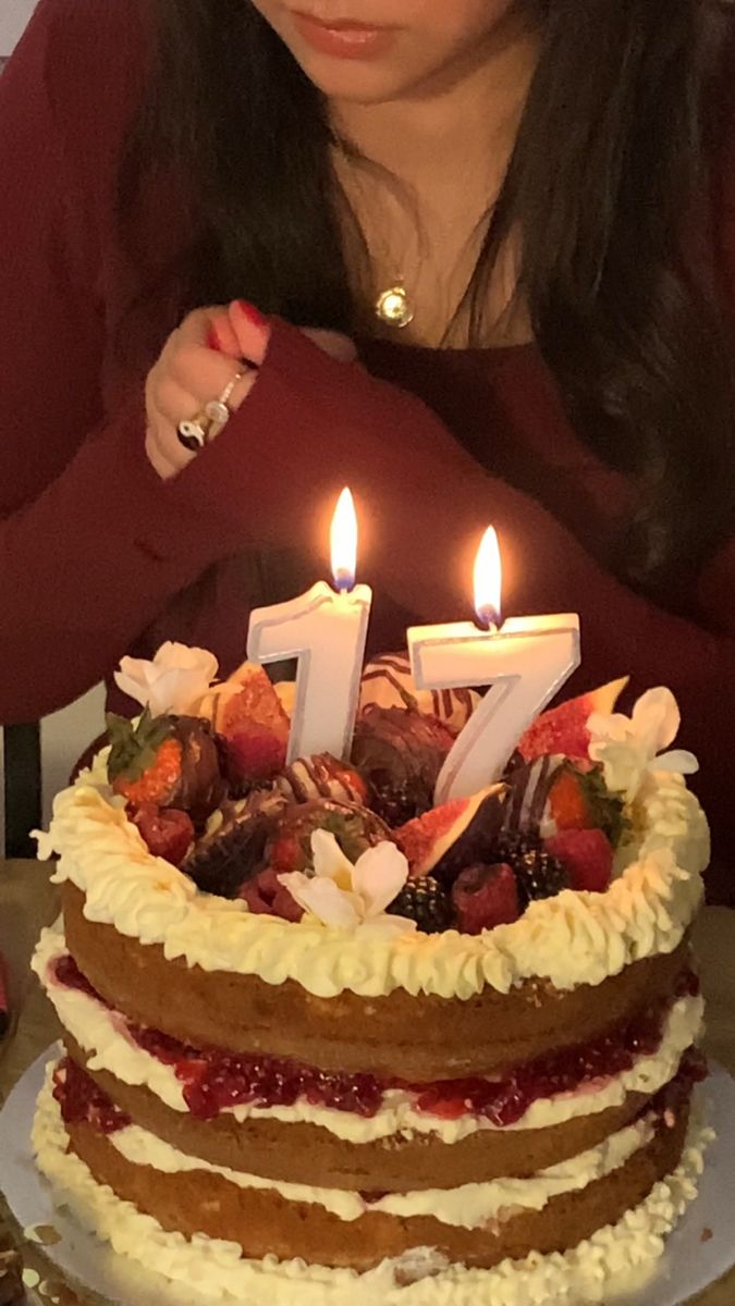 a woman sitting in front of a cake with lit candles on it and looking at the camera