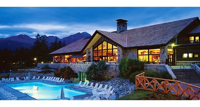 an outdoor swimming pool surrounded by lawn chairs at night with mountains in the backgroud