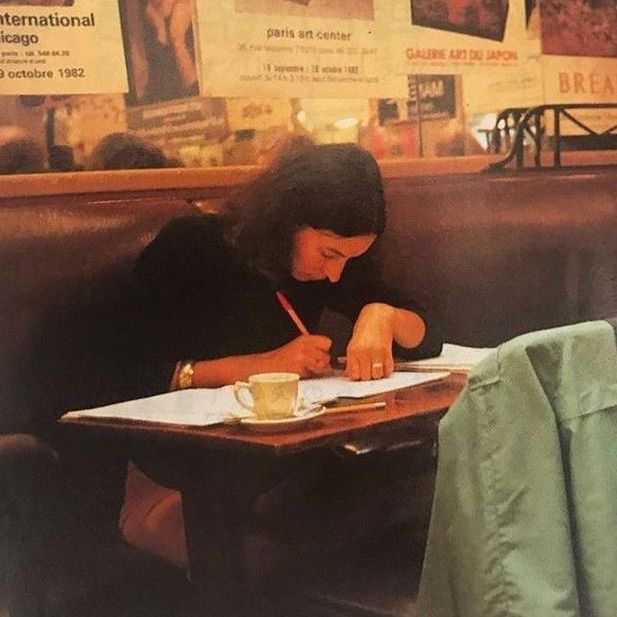 a woman sitting at a table writing on a piece of paper with a cup of coffee in front of her