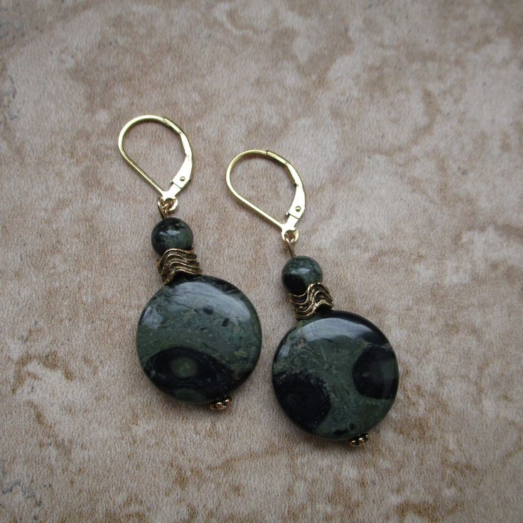 These green stone earrings are made with Kambaba stone. Kambaba is two shades of green, and each pattern is unique. You will love wearing these brilliant green lever-back earrings. *Kambaba coin-shaped stone: measures .7 inch in diameter *Accents: Gold-plated beads and a small, round Kambaba stone *14k gold-filled lever backs *Approximate length of earrings: 2 inches Green Jade Earrings With Natural Stones, Green Lever Back Earrings As A Gift, Green Earrings With Natural Stones As Gift, Bohemian Round Jade Earrings, Handmade Green Round Earrings, Green Brass Earrings With Natural Stones, Handmade Dark Green Round Jewelry, Green Stone Earrings, Kazuri Beads