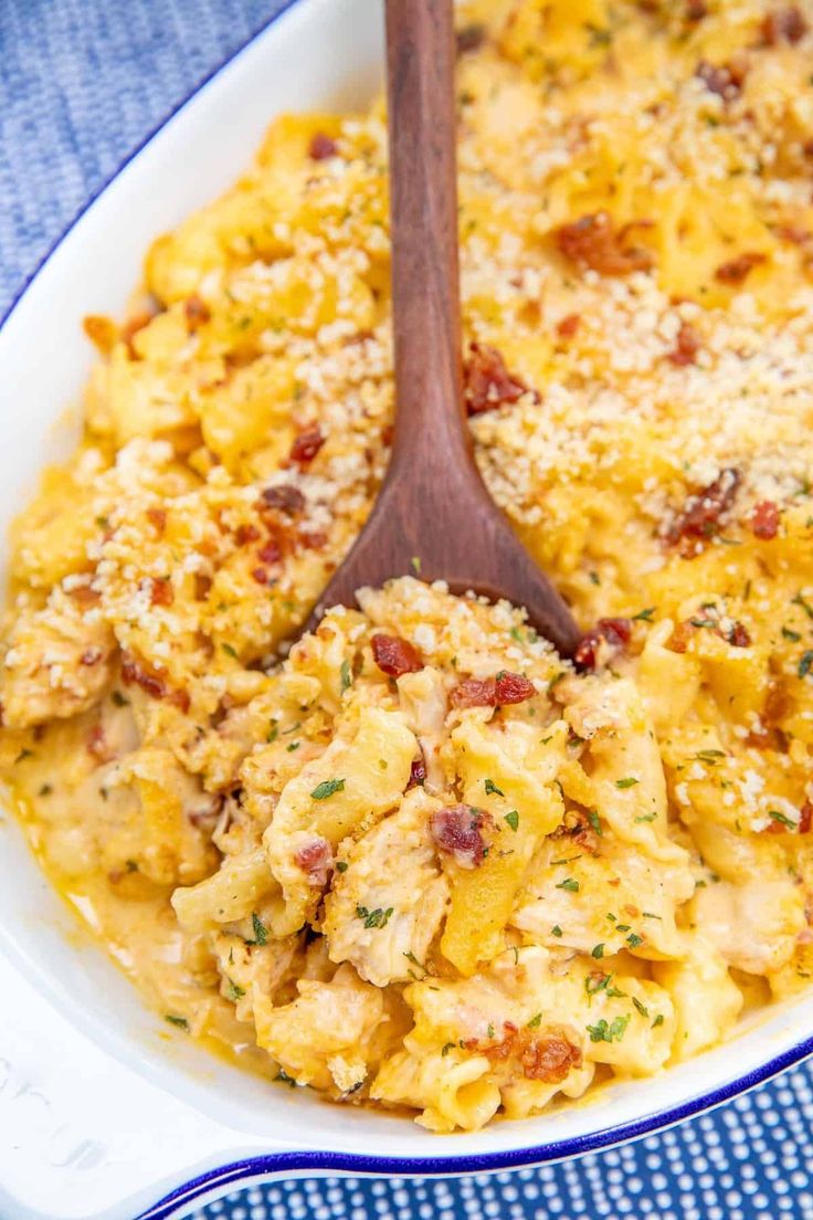 a casserole dish filled with macaroni and cheese, topped with a wooden spoon