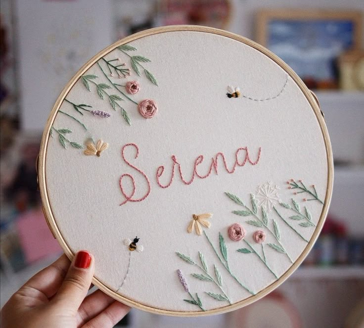 someone is holding up a hand embroidered name on a white hoop with pink flowers and green leaves