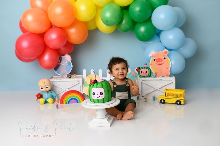 a baby is sitting in front of a cake with animals and rainbows on it