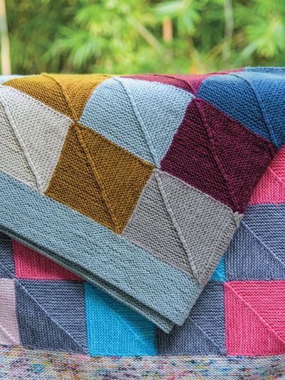 a multicolored blanket sitting on top of a couch next to a planter