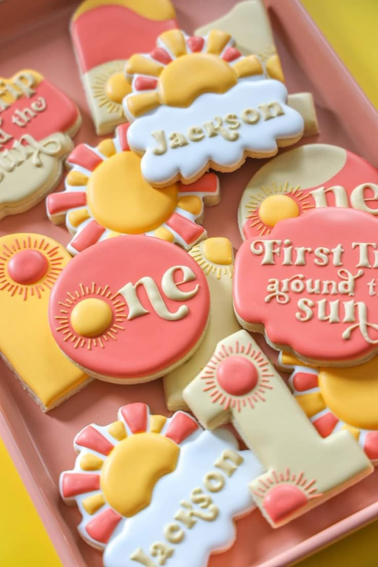 some decorated cookies are sitting on a pink tray with the words first time around the sun