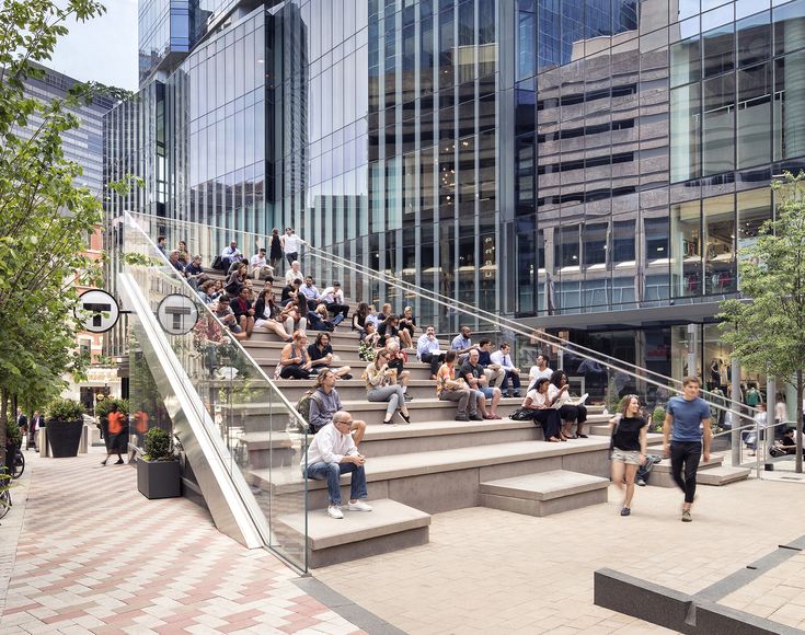 many people are walking up and down the stairs in front of some tall buildings with glass windows