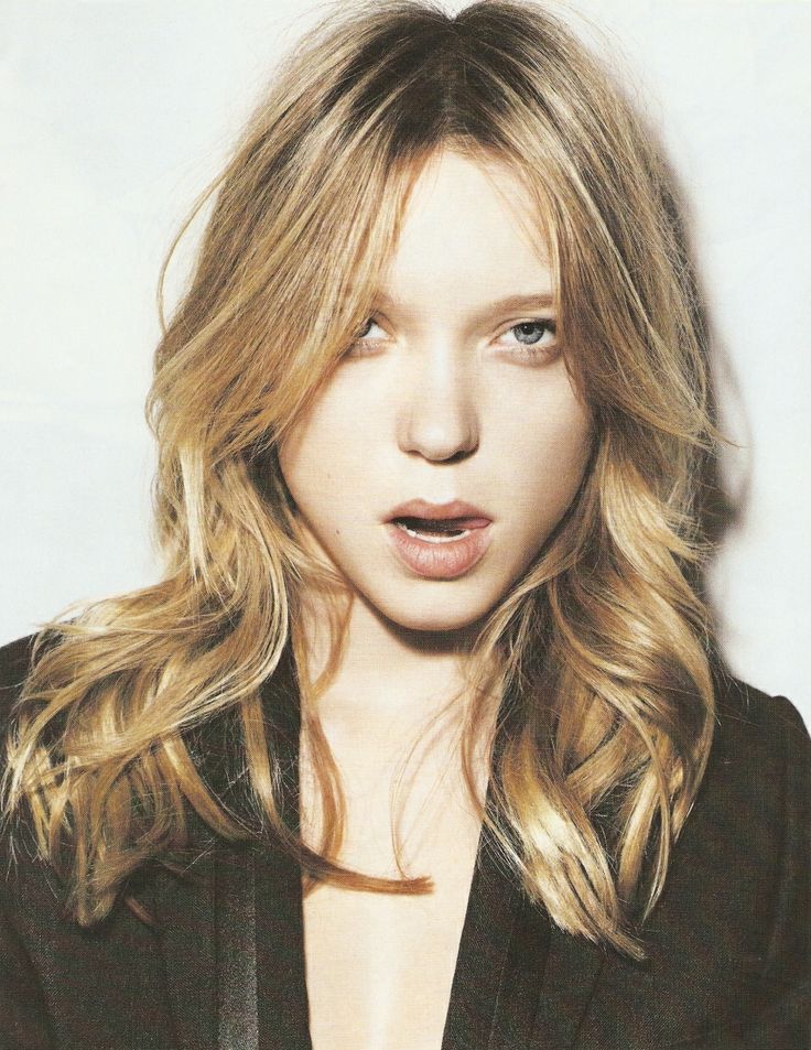 a woman with long blonde hair and blue eyes posing for a photo in front of a white background