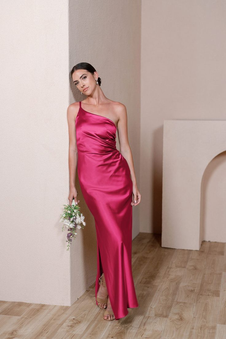 a woman in a long pink dress standing next to a wall with her hand on her hip