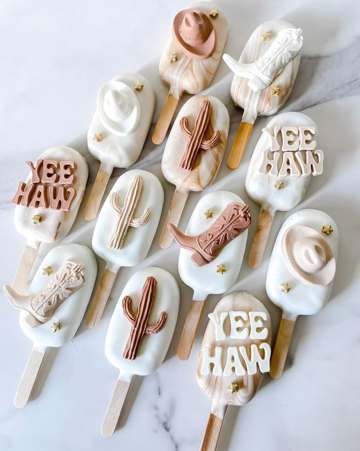 a table topped with pops covered in white frosting and desert themed icing next to wooden utensils