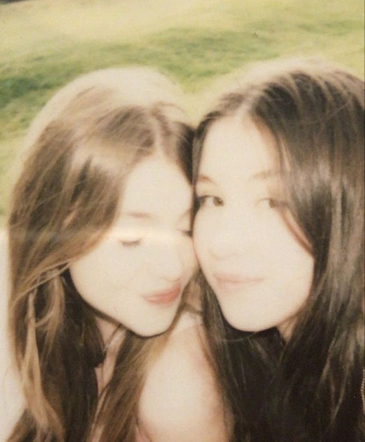 two young women are posing for a photo in front of the grass and trees with their heads close to each other