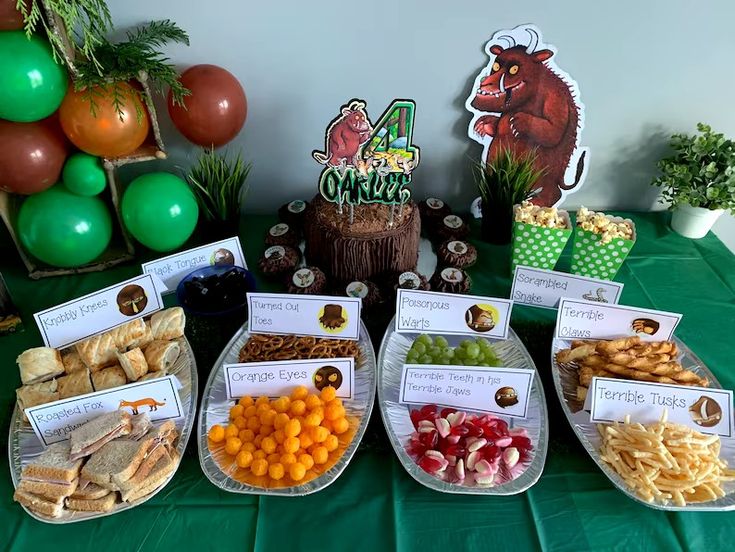 a table topped with lots of food and desserts next to green tables covered in balloons