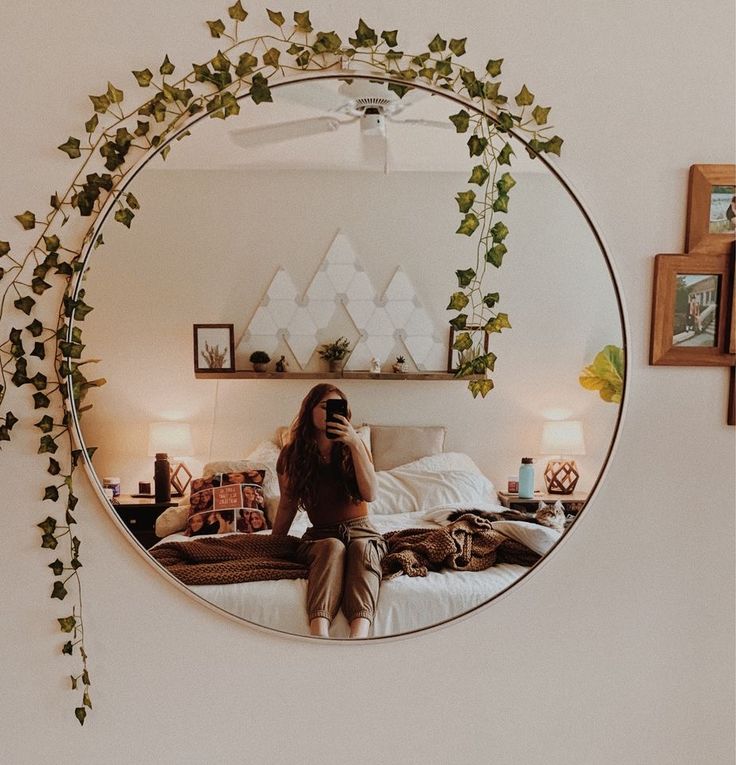 a woman sitting on a bed in front of a mirror with ivy growing over it