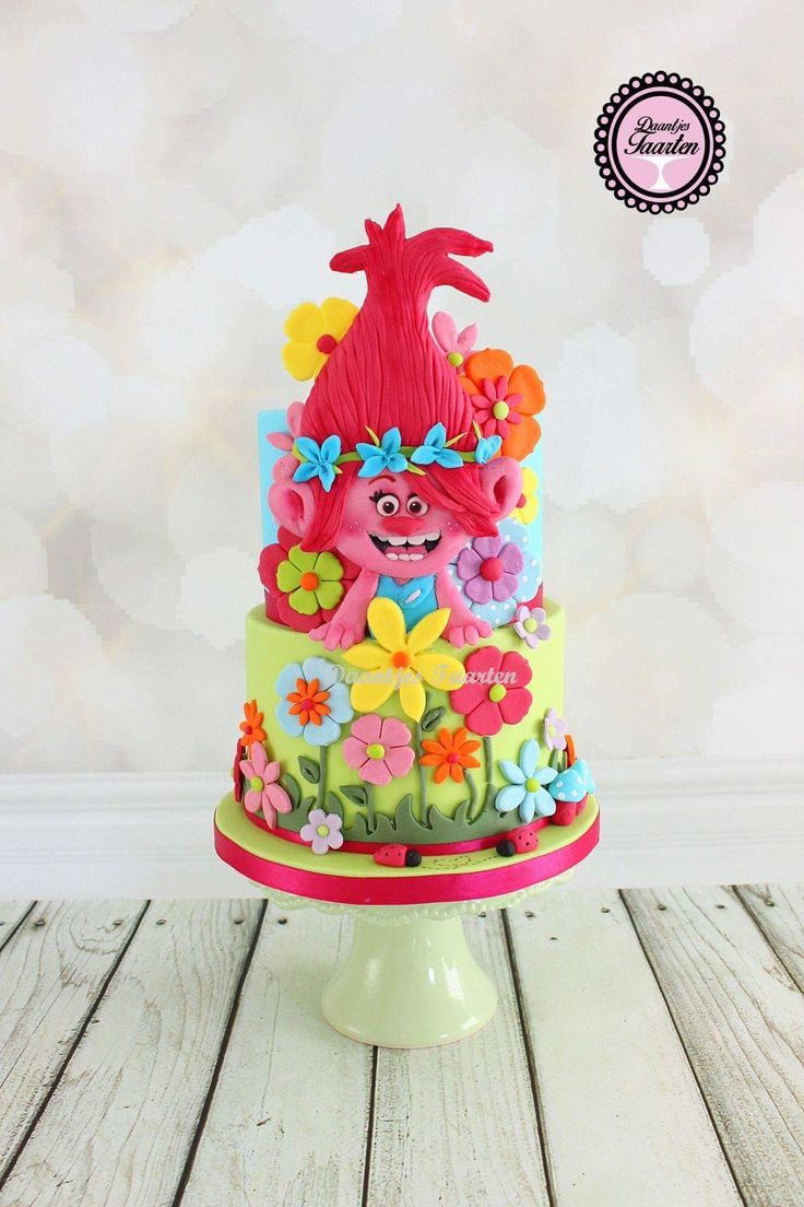 there is a colorful cake decorated with flowers and a troll on the top, sitting on a table