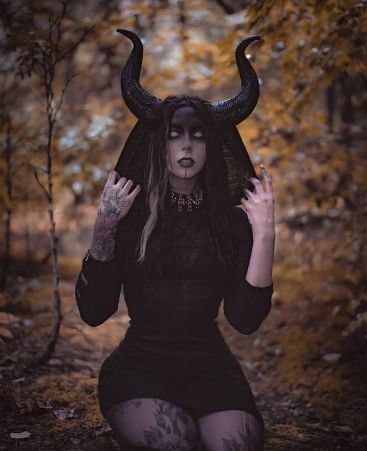 a woman with horns on her head sitting in the woods