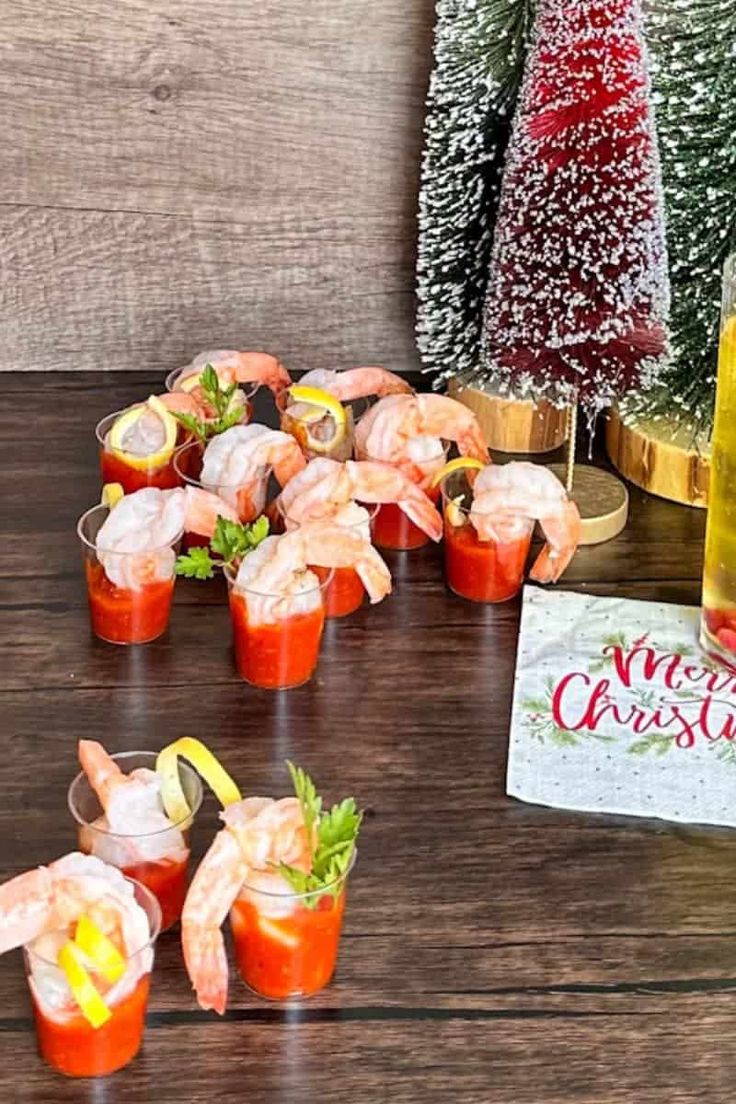 shrimp cocktails and appetizers on a table with christmas trees in the background