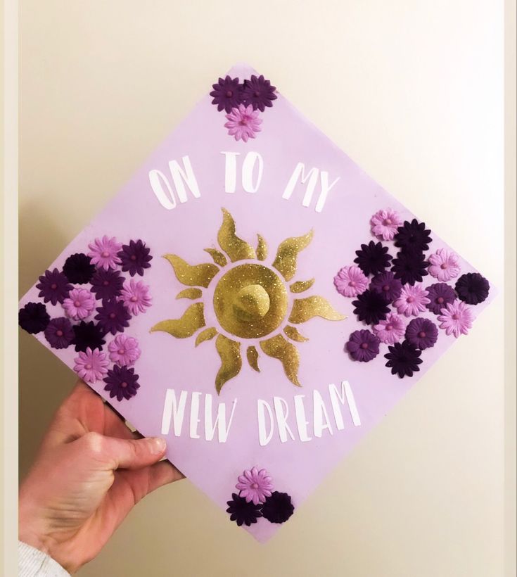 someone holding up a purple and gold graduation cap with flowers on it that says, on to my new dream