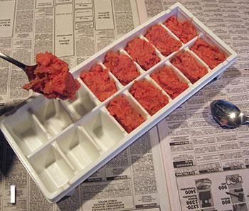 an ice cube tray filled with red food next to a spoon on top of newspaper