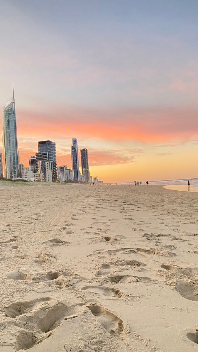 a beach with footprints in the sand and skyscrapers in the background