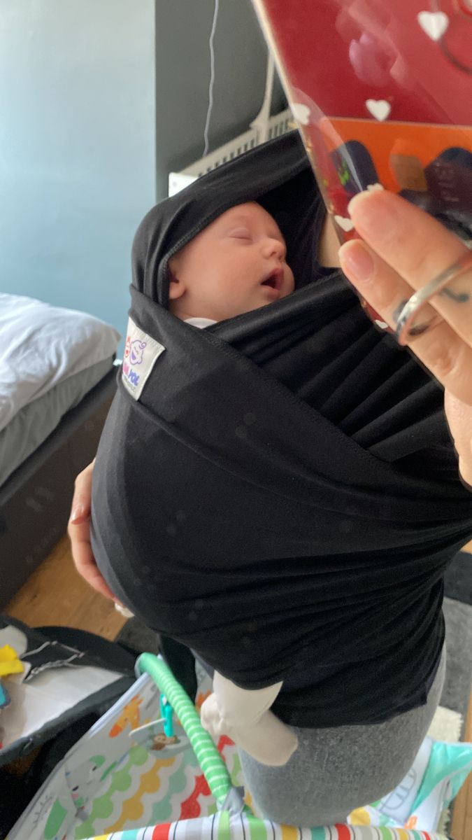 a person holding a baby wrapped in a black wrap and taking a photo with a cell phone