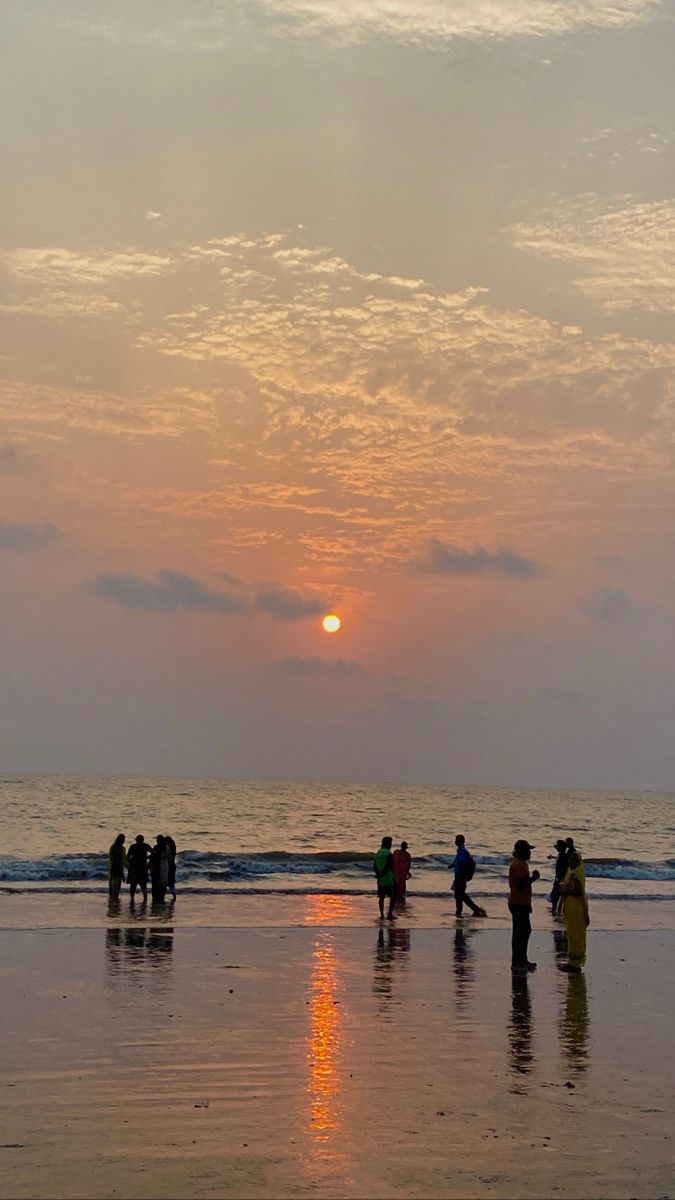 people are standing on the beach watching the sun go down