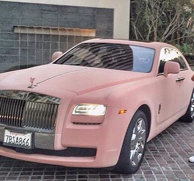 a man standing next to a pink rolls royce parked in front of a garage door