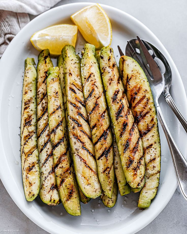 grilled zucchini on a white plate with lemon wedges and a fork