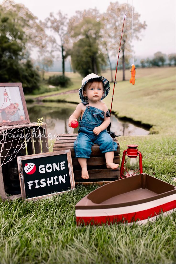 a little boy sitting on top of a box next to a fishing pole and other items