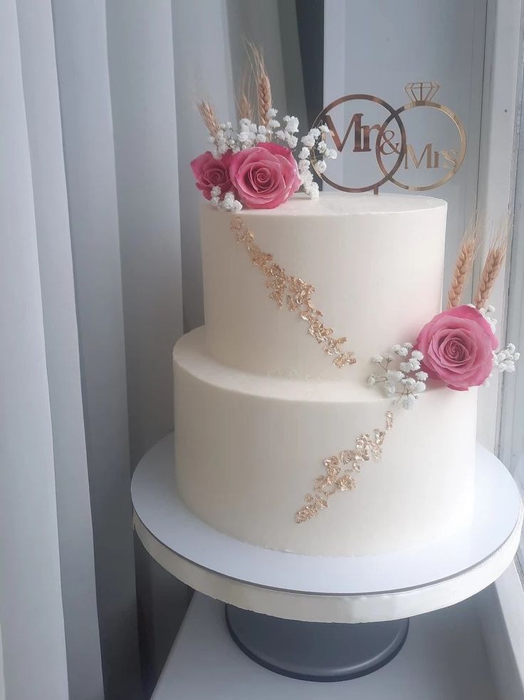 a three tiered wedding cake with pink roses on top and gold lettering that says mr and mrs