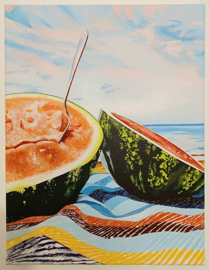 a watermelon cut in half sitting on top of a beach towel next to the ocean