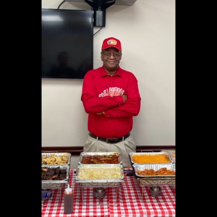 a man standing in front of several trays of food on a table with a red and white checkered tablecloth