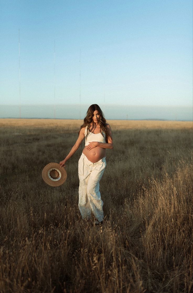 a pregnant woman standing in a field holding a frisbee