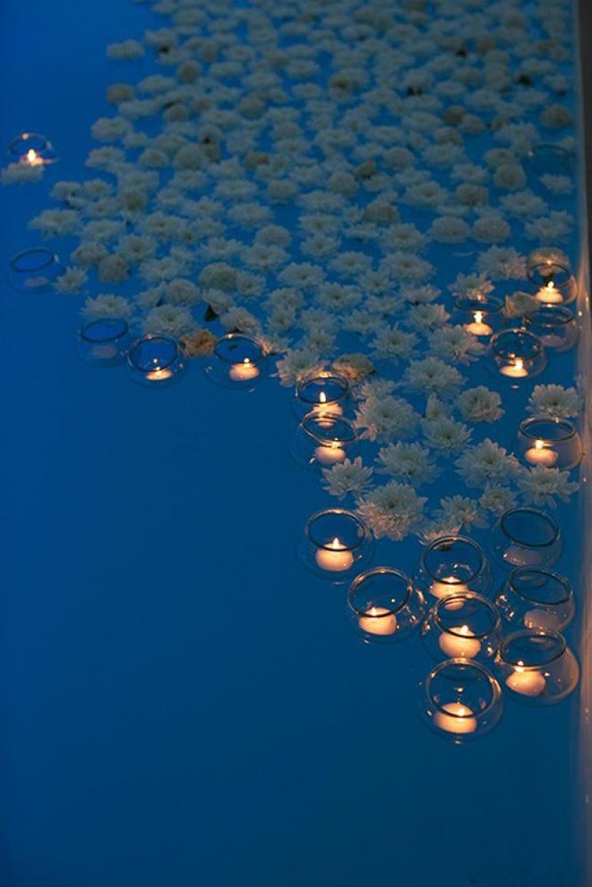 many lit candles are on the table with flowers in them and floating water behind it