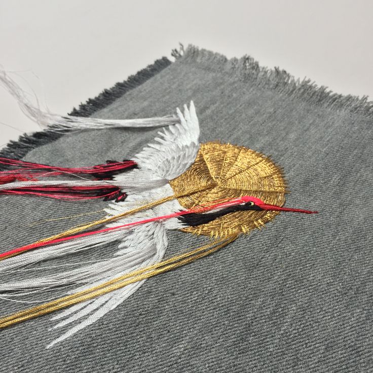 two white and red feathers sitting on top of a piece of gray fabric with fringes