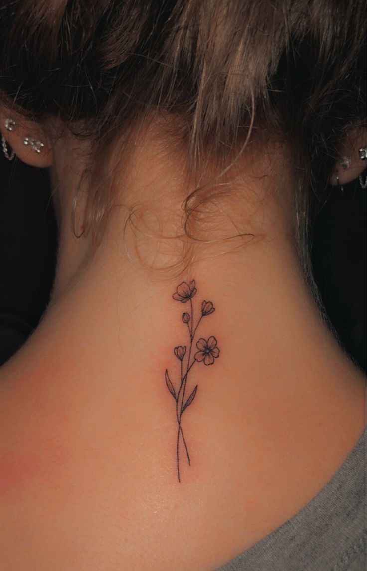 a woman's back neck with a small flower tattoo on her left side ribcage