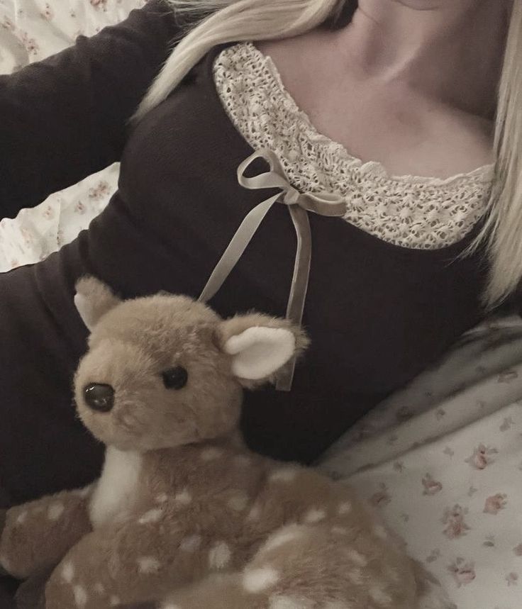 a woman laying in bed with a stuffed animal next to her stomach and wearing a brown shirt