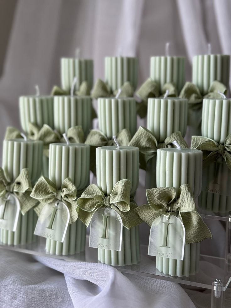 many candles with bows are lined up on a white table cloth and tied in green ribbon