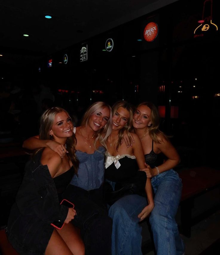 four beautiful young women sitting next to each other at a bar and posing for the camera