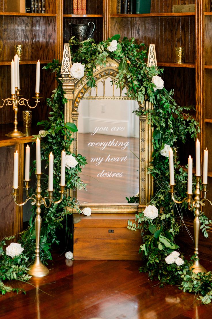 a wedding arch decorated with greenery and candles in front of a book shelf filled with books