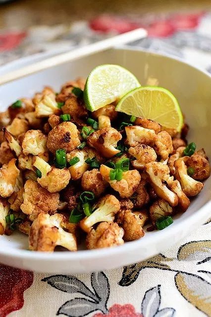 a white bowl filled with cauliflower and limes next to chopsticks